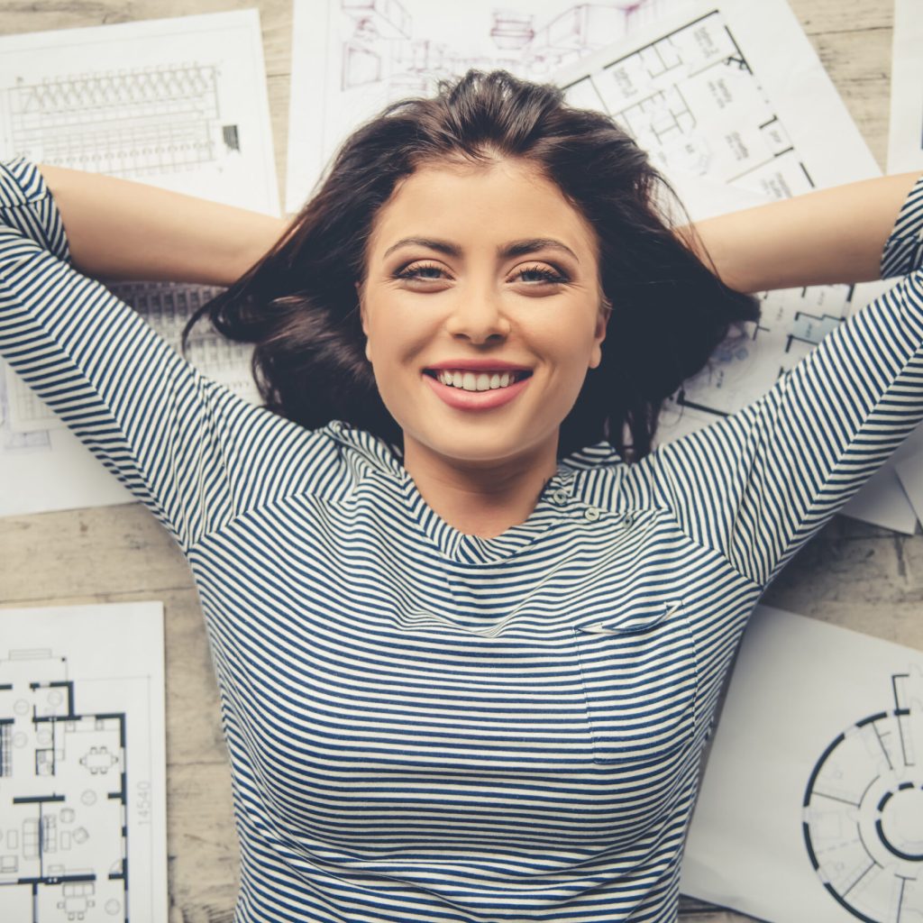 Top view of beautiful business lady in casual clothes looking at camera and smiling while lying on the floor among documents