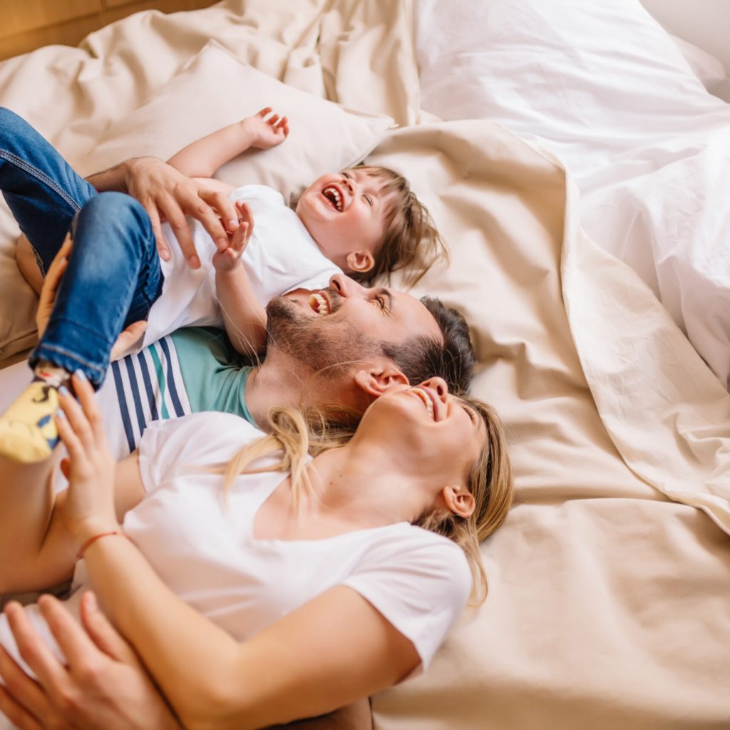 Young couple with their daughter are laughing while they lying on bed in bedroom