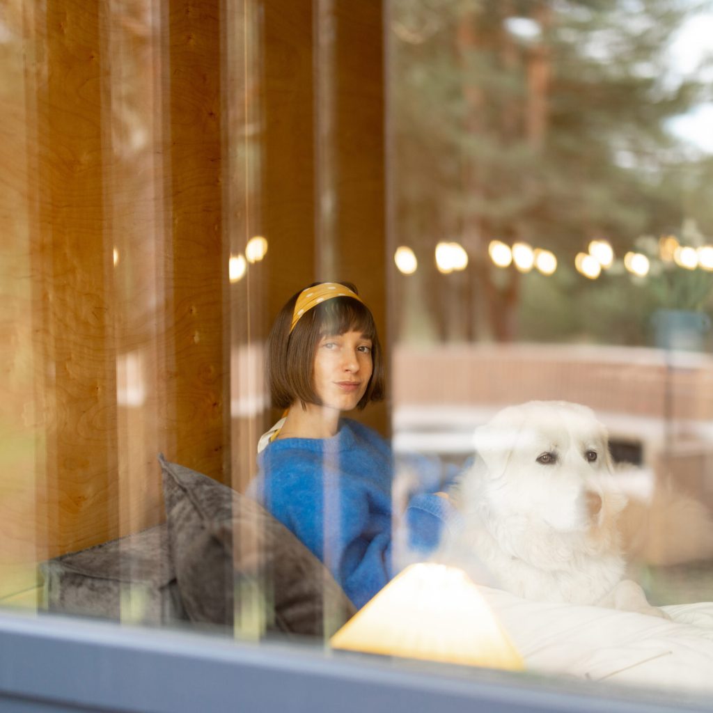 Woman with dog sitting together by the window in wooden cottage, view through the window.